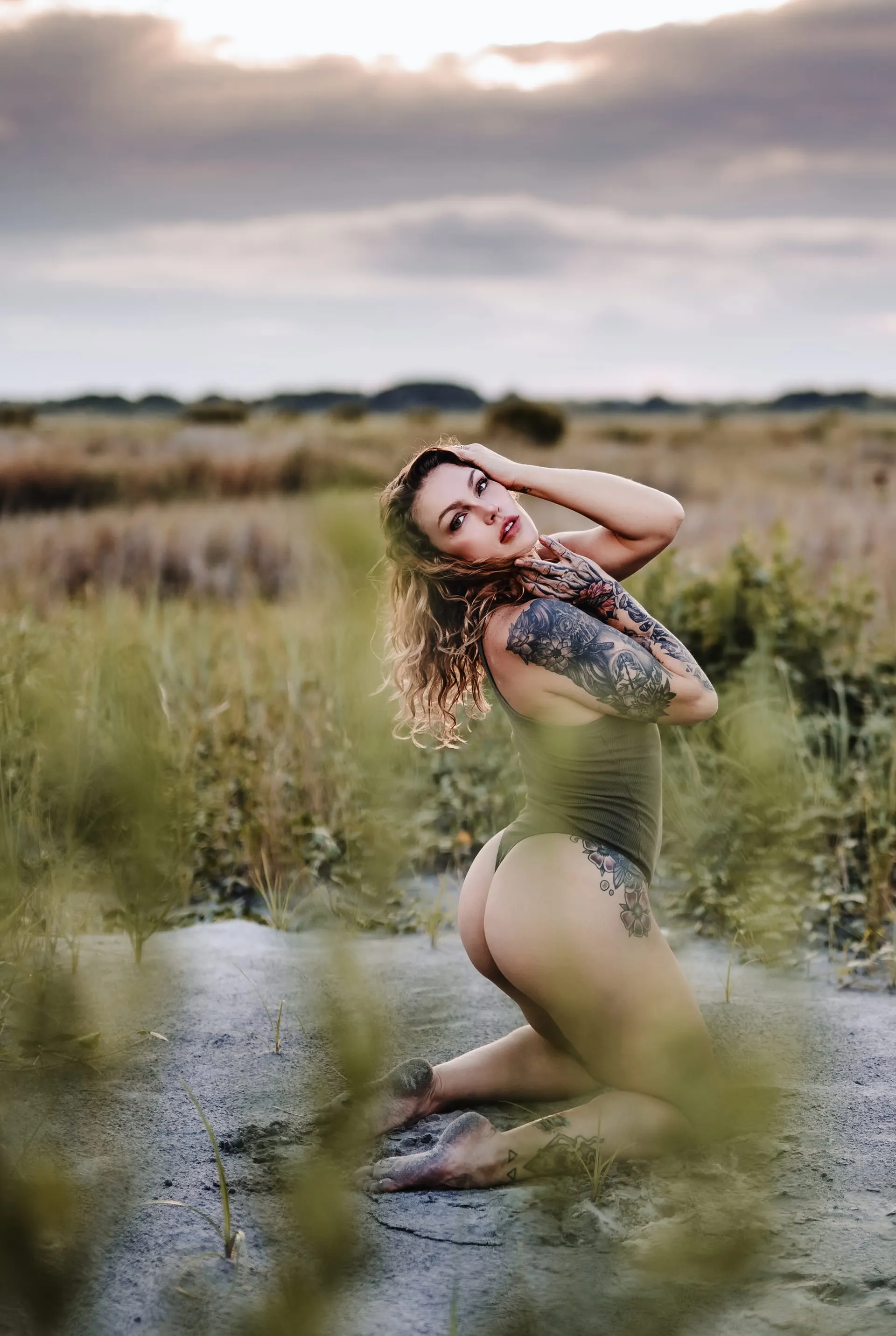 Soft-focus grasses frame a woman kneeling on sand at dusk