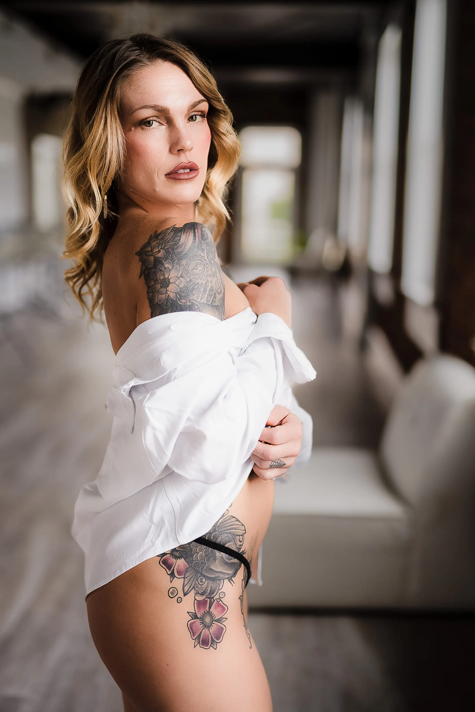 Oversized white shirt slipping off one shoulder, glancing back in a sunlit loft