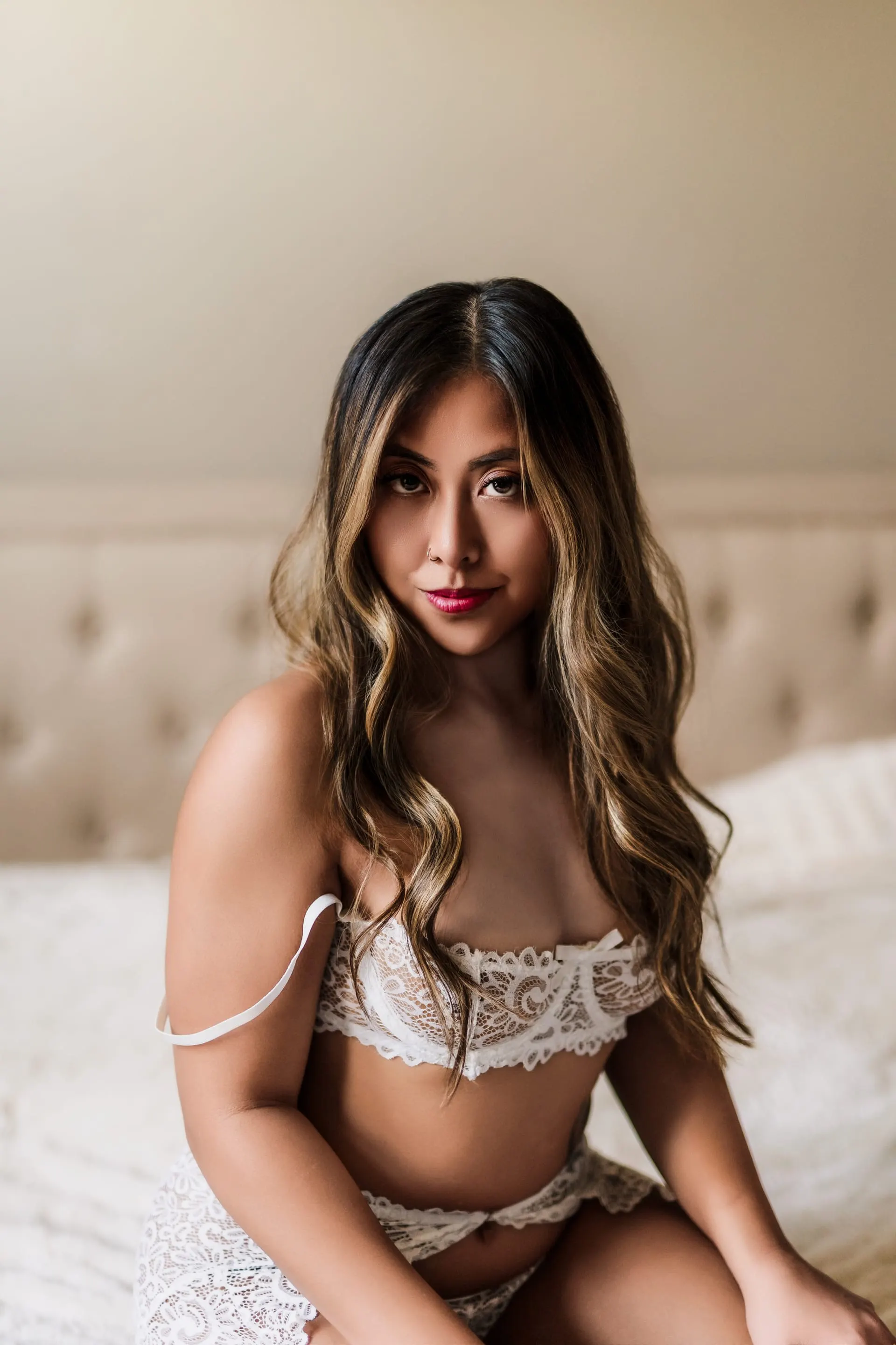 Close portrait of a woman in white lace seated on a softly lit bed