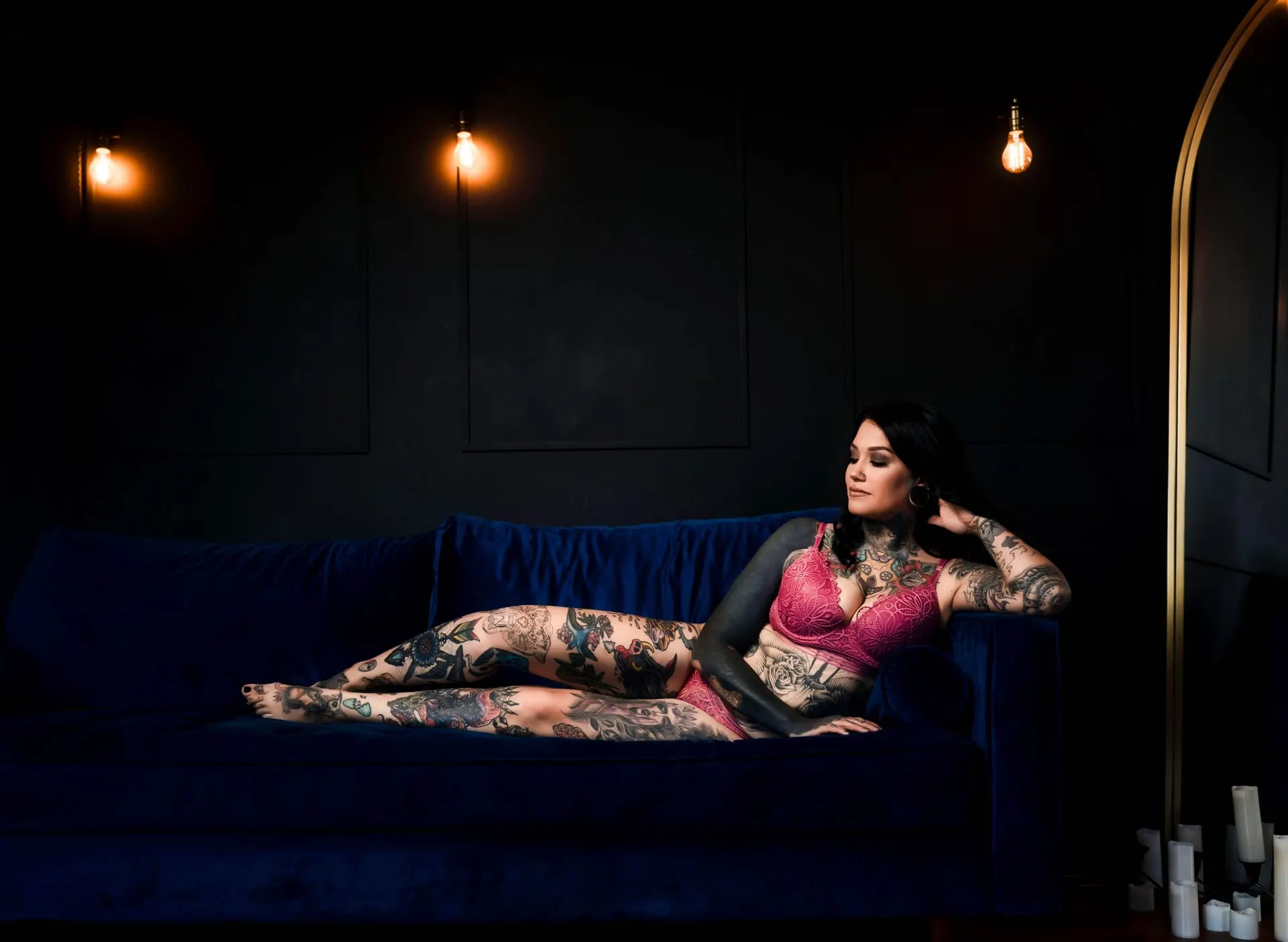 Woman in pink lace lounging on a navy sofa beneath glowing bulbs
