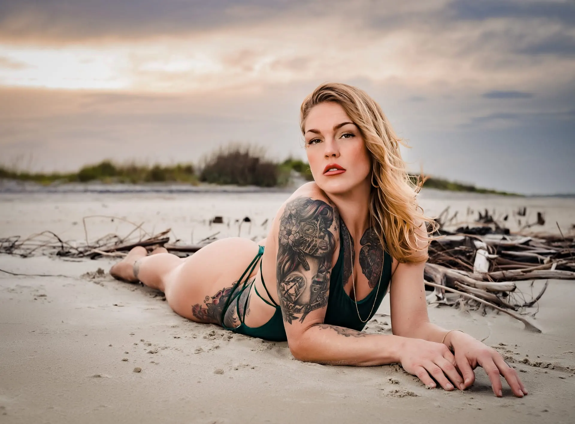 Woman reclining on the sand at sunset with driftwood behind her