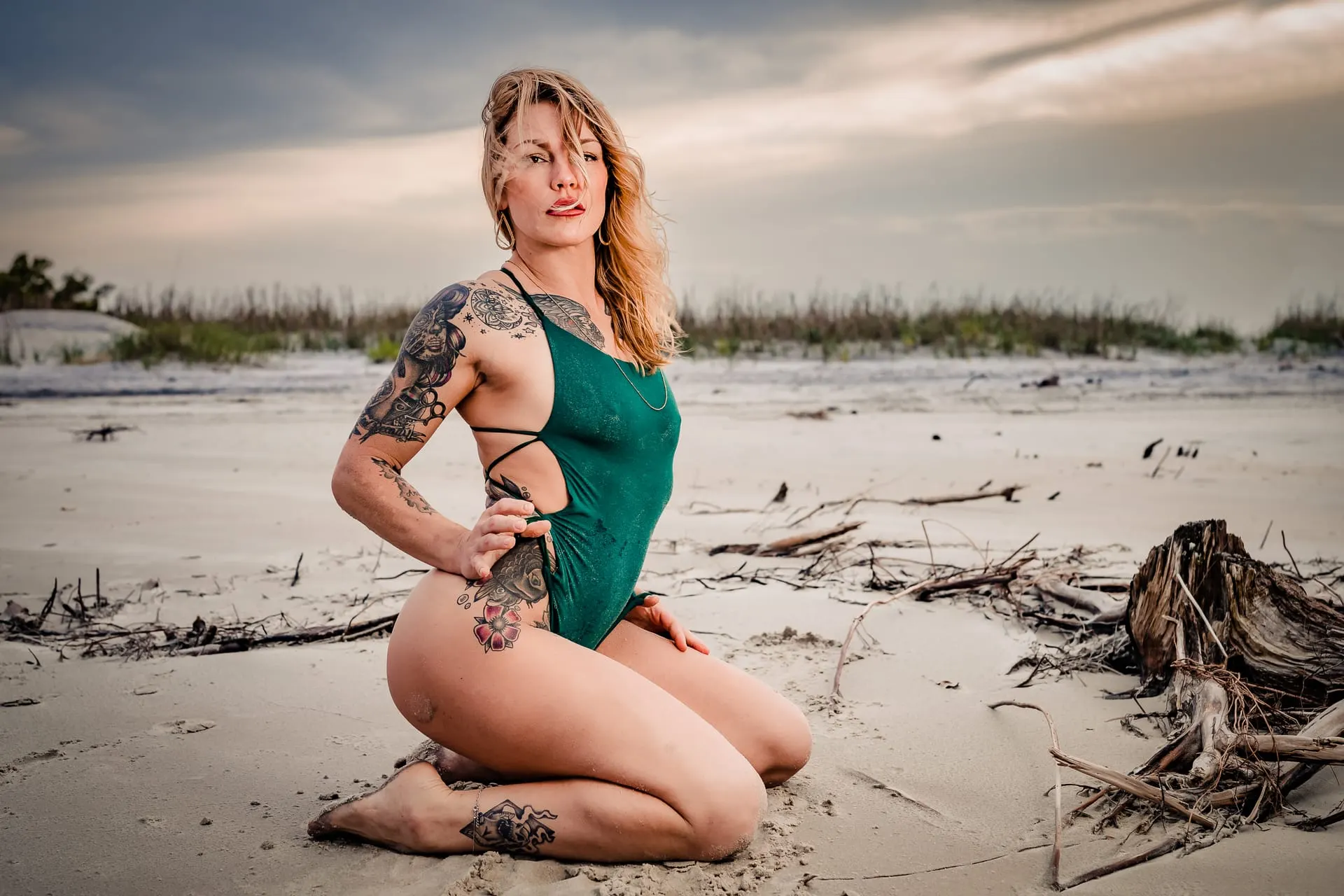 Woman in a green cutout one-piece kneeling on a windswept beach